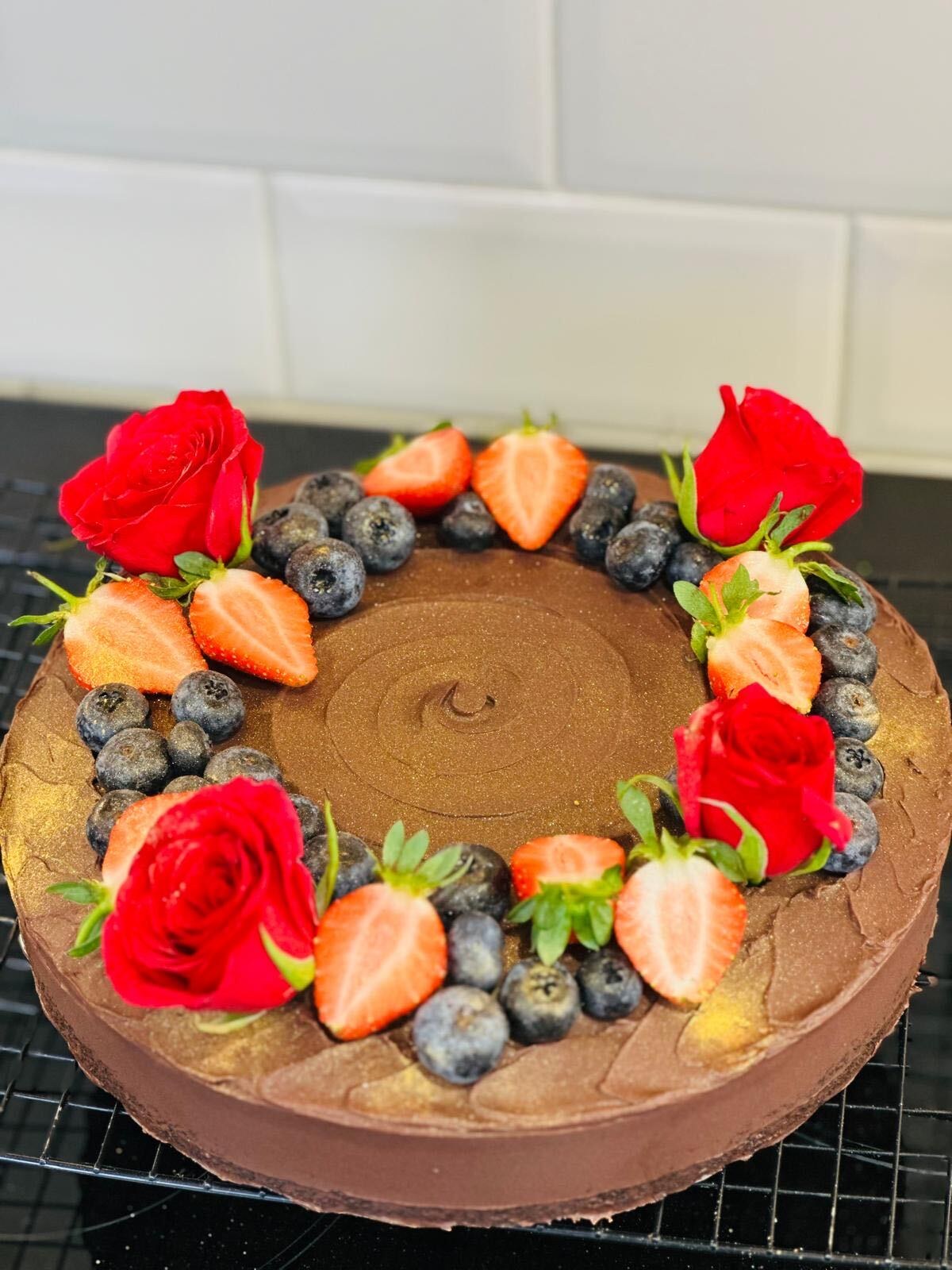Teff and date torte with chocolate ganache, decorated with red roses, strawberries and blueberries